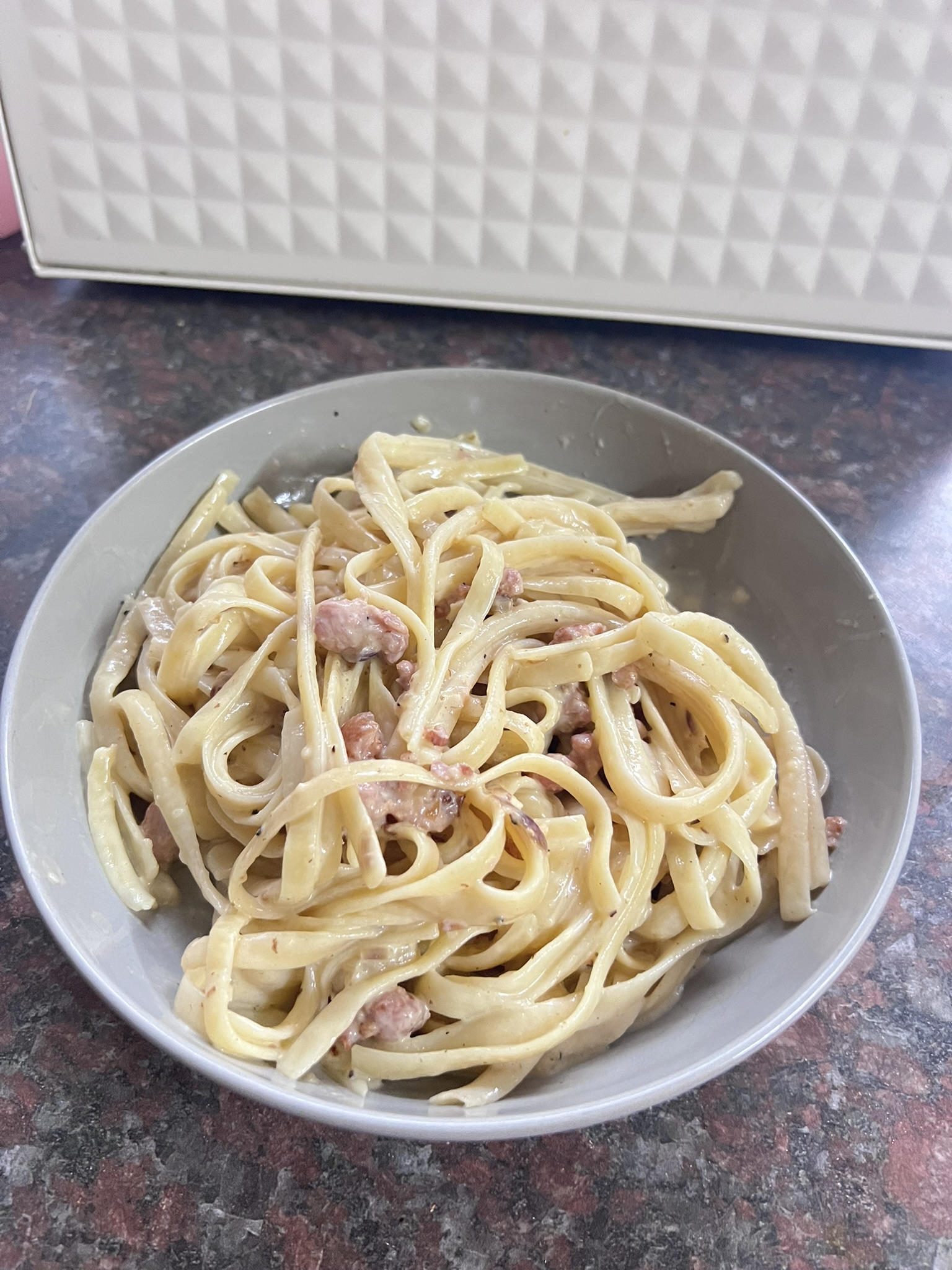 Bowl of creamy bacon carbonara with black pepper and grated parmesan